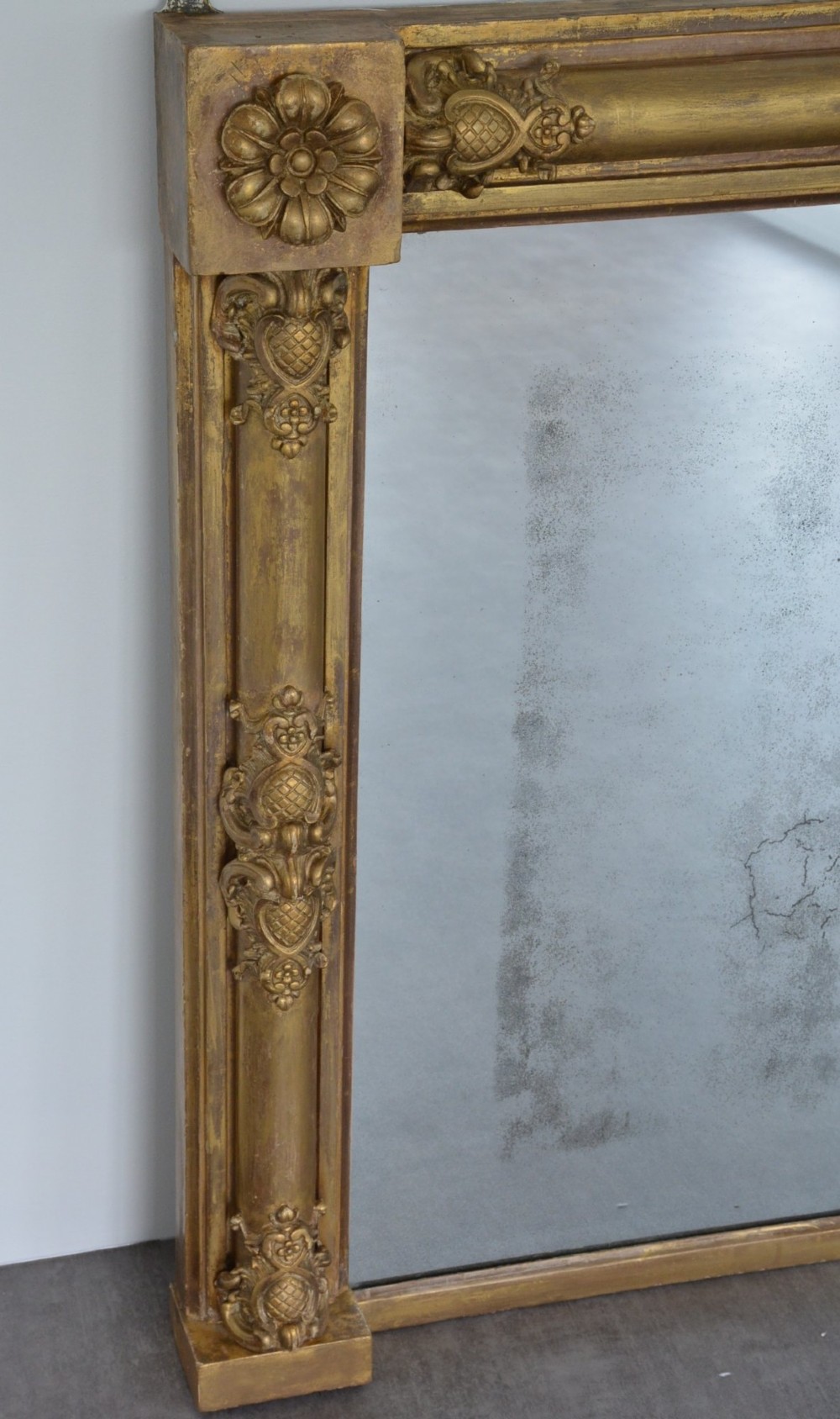 A large horizontal Regency style mirror featuring a gilded frame decorated with corner rosettes and floral mouldings enclosing foxed mirror glass. View IX