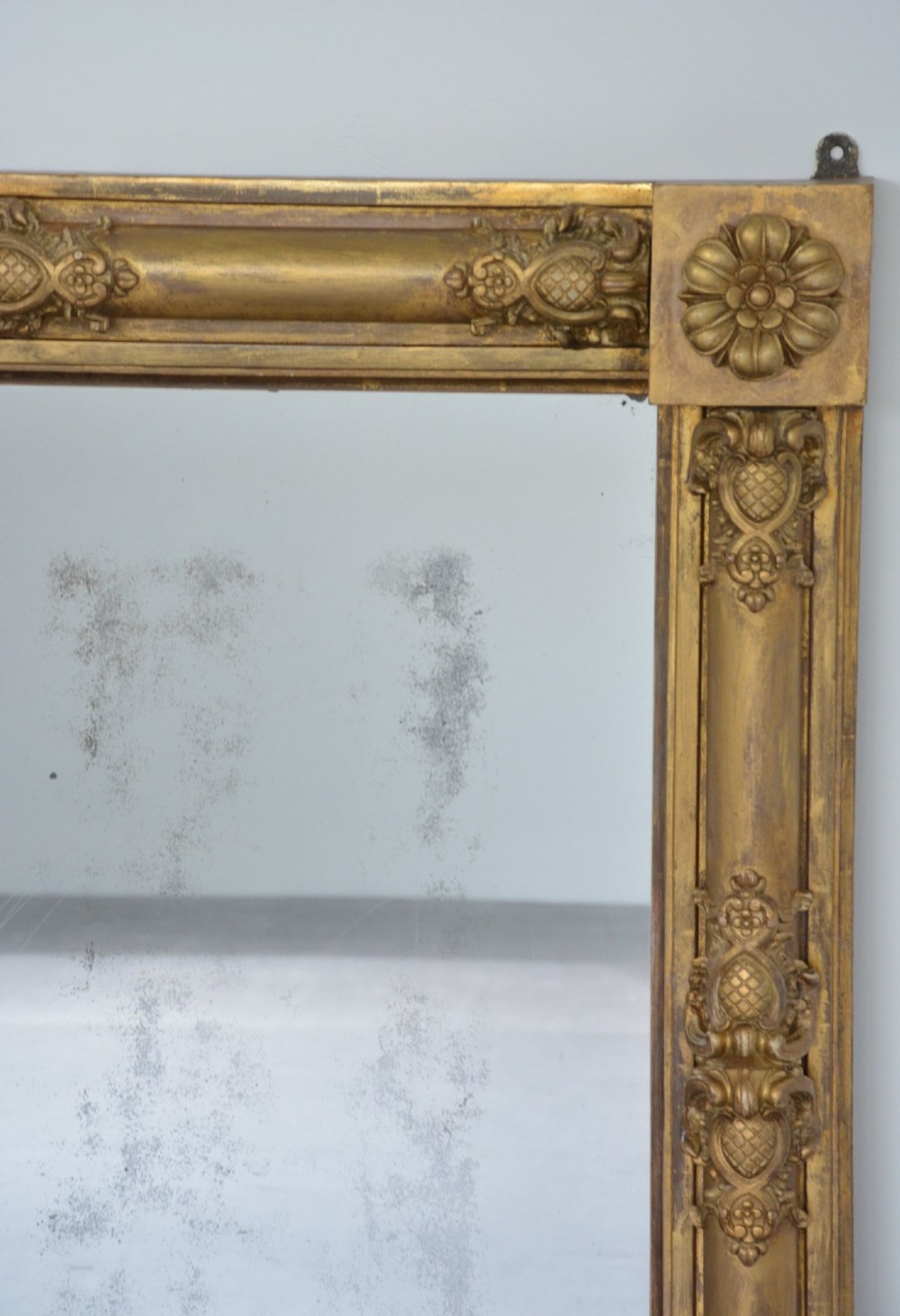 A large horizontal Regency style mirror featuring a gilded frame decorated with corner rosettes and floral mouldings enclosing foxed mirror glass. View X