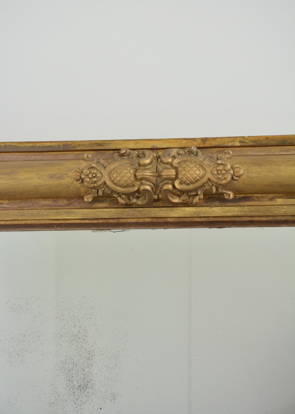 A large horizontal Regency style mirror featuring a gilded frame decorated with corner rosettes and floral mouldings enclosing foxed mirror glass. View XII