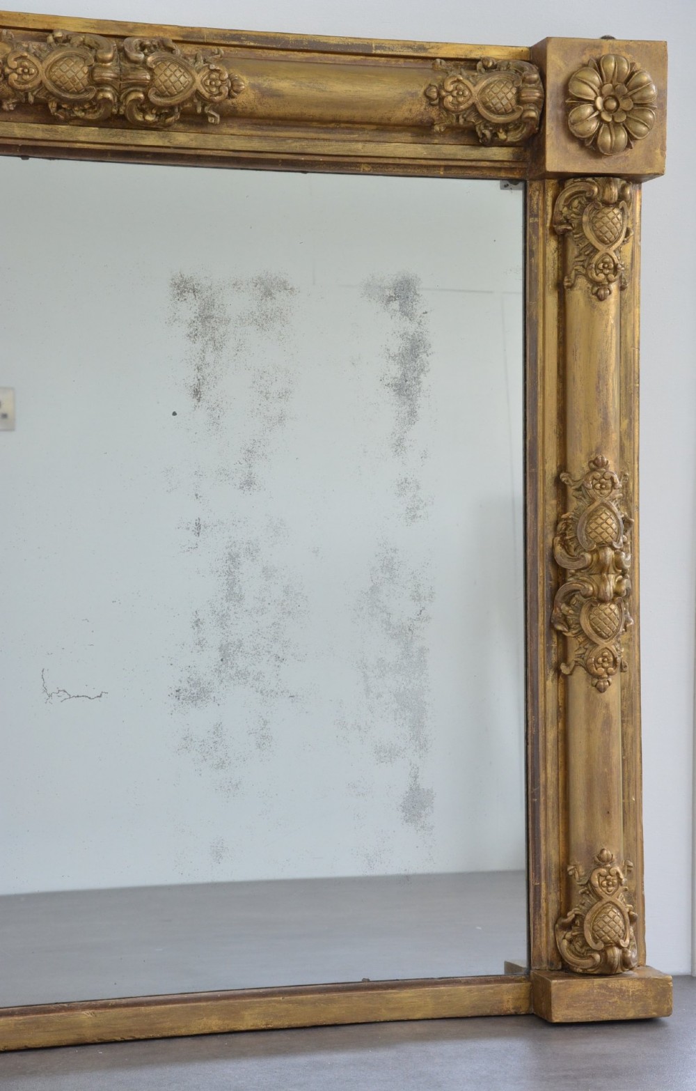 A large horizontal Regency style mirror featuring a gilded frame decorated with corner rosettes and floral mouldings enclosing foxed mirror glass. View XIII
