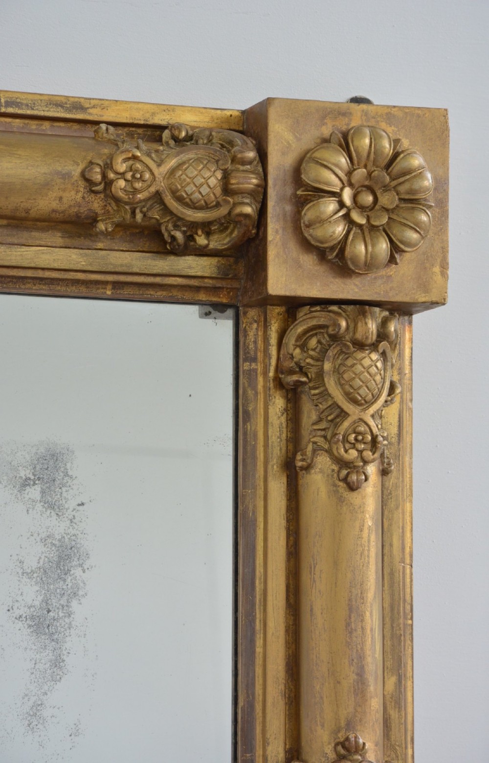 A large horizontal Regency style mirror featuring a gilded frame decorated with corner rosettes and floral mouldings enclosing foxed mirror glass. View XIV