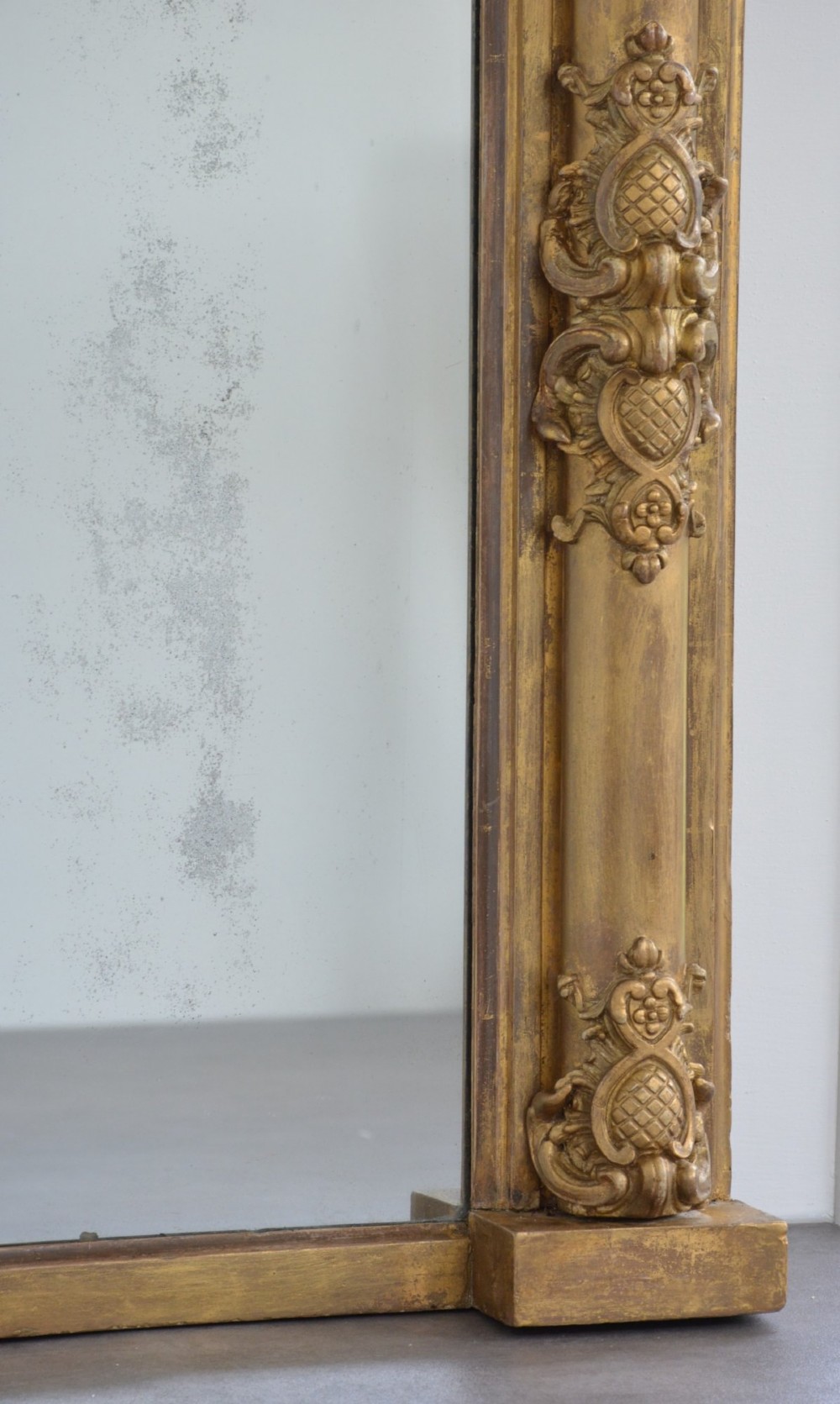 A large horizontal Regency style mirror featuring a gilded frame decorated with corner rosettes and floral mouldings enclosing foxed mirror glass. View XV