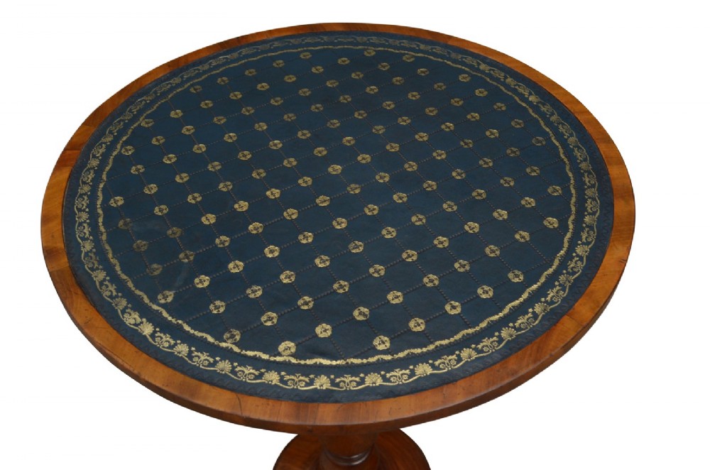 A William IV mahogany circular lamp table featuring a dark blue gilt-tooled leather inset top supported by a turned pedestal stem on a tri-form scroll-foot base. View II