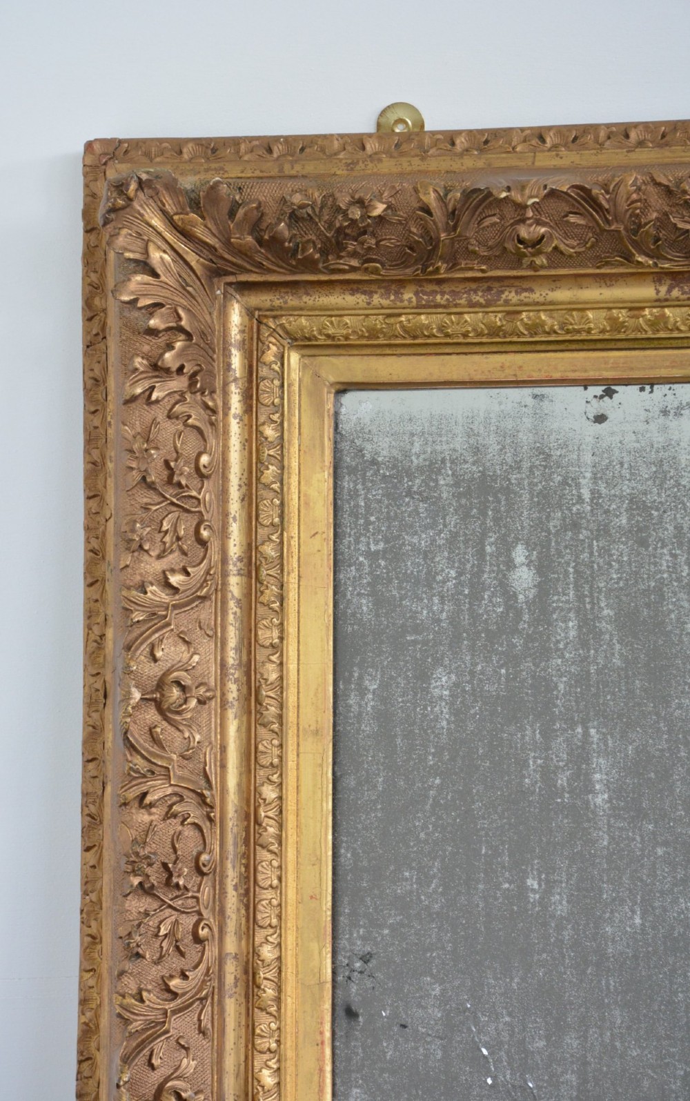 A rectangular 19th-century French giltwood wall mirror featuring an ornate carved frame and heavy antique foxing across the glass plate. View VII