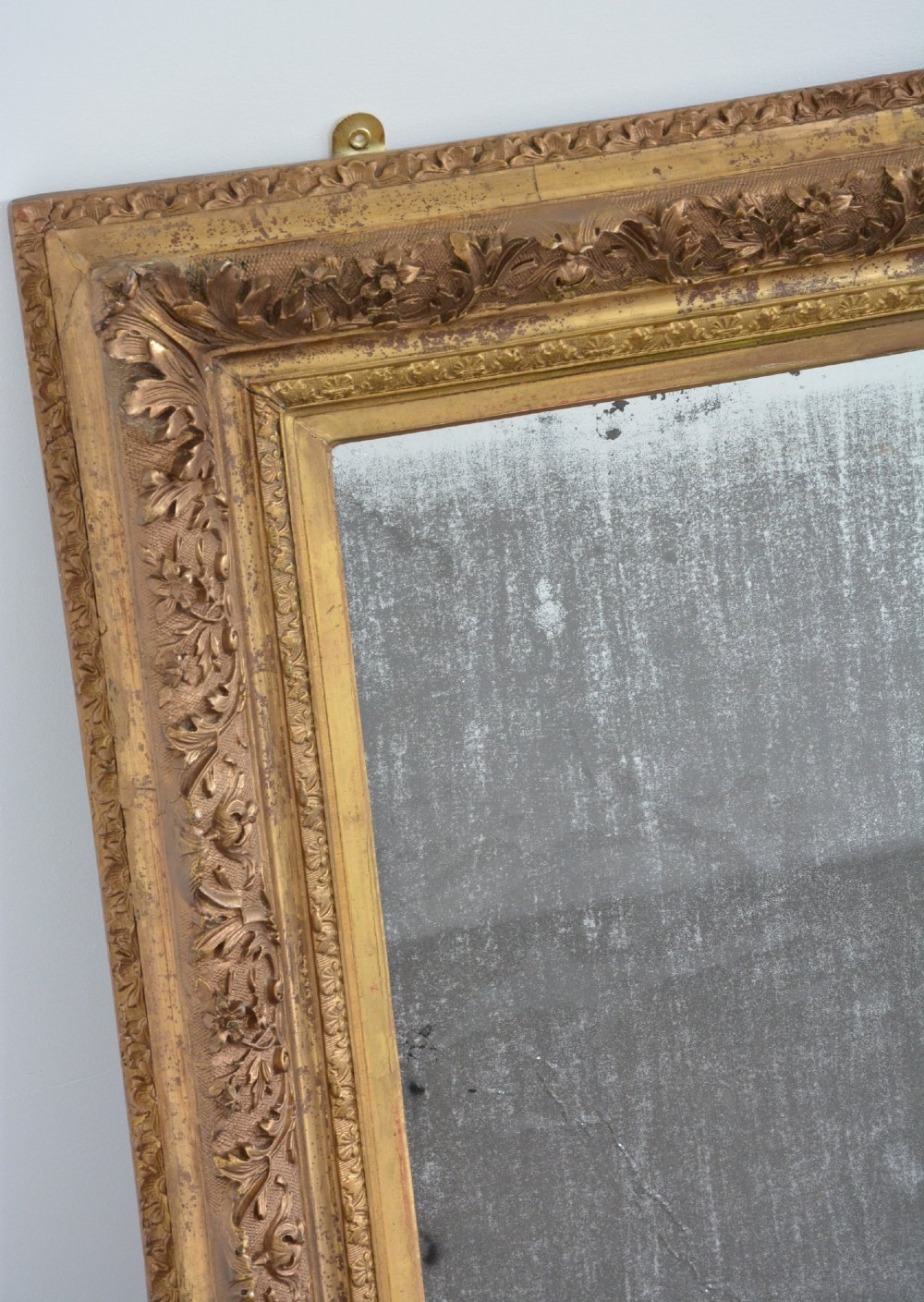 A rectangular 19th-century French giltwood wall mirror featuring an ornate carved frame and heavy antique foxing across the glass plate. View X