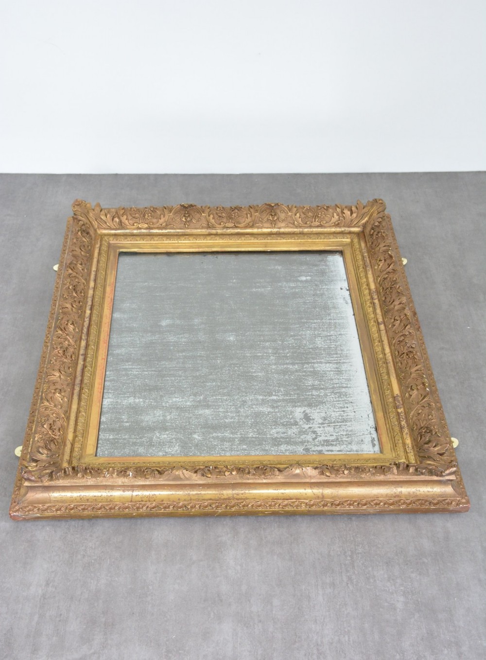A rectangular 19th-century French giltwood wall mirror featuring an ornate carved frame and heavy antique foxing across the glass plate. View XIV