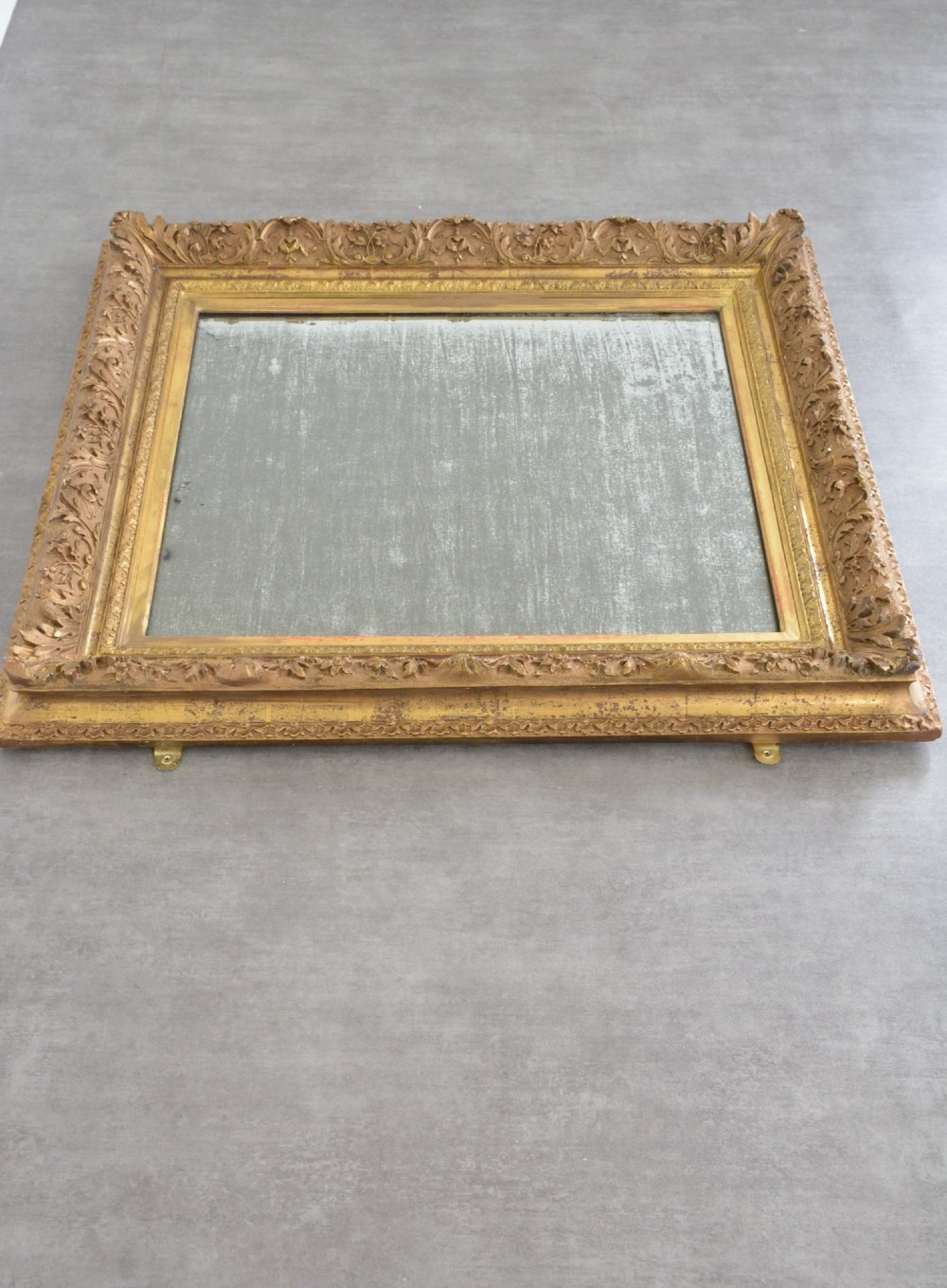 A rectangular 19th-century French giltwood wall mirror featuring an ornate carved frame and heavy antique foxing across the glass plate. View XV