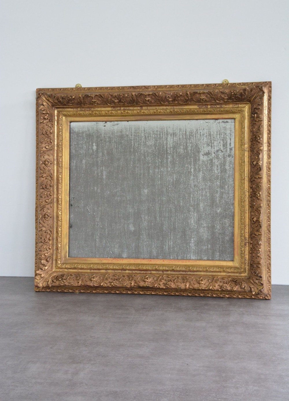 A rectangular 19th-century French giltwood wall mirror featuring an ornate carved frame and heavy antique foxing across the glass plate. View II