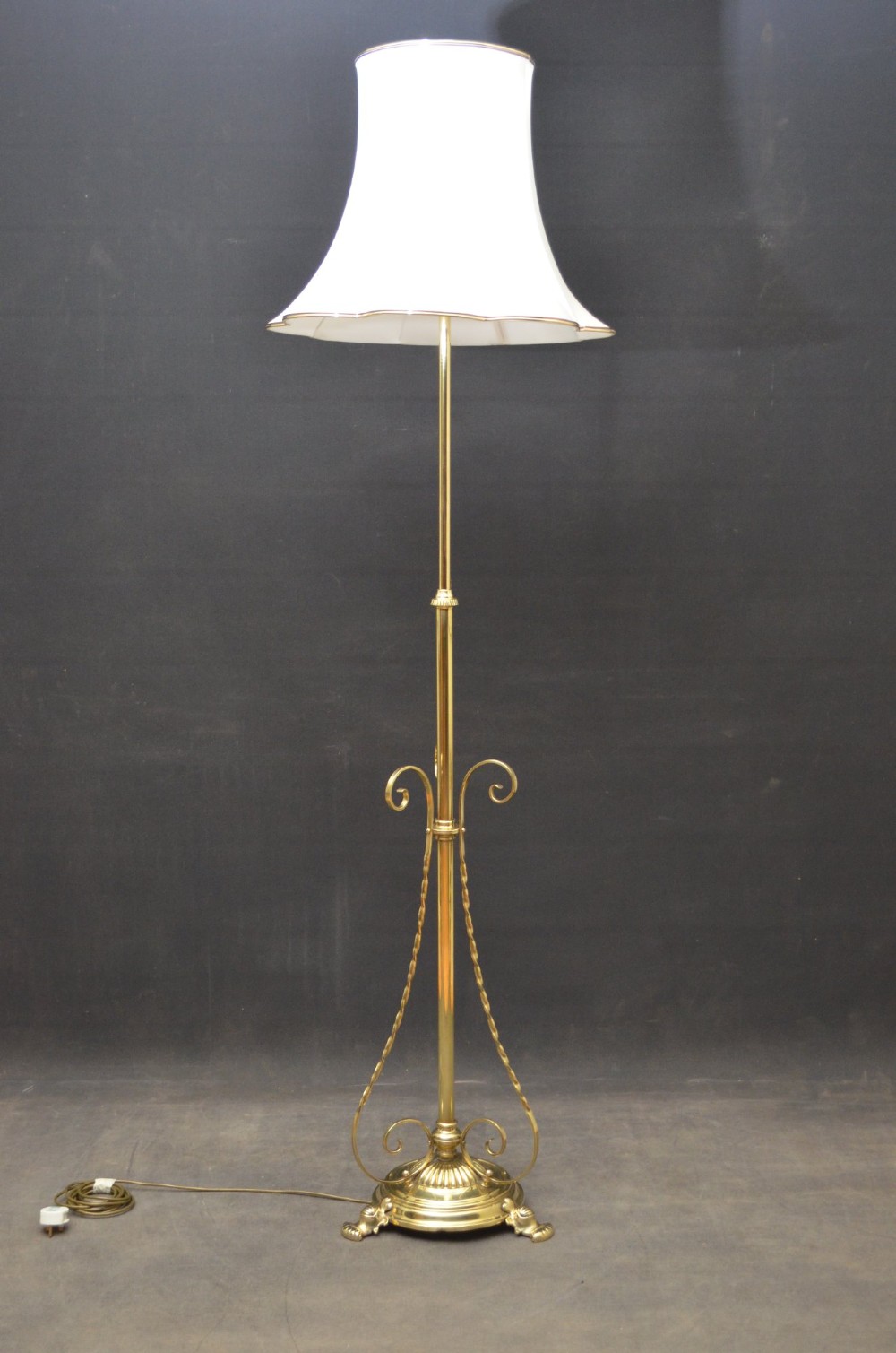 An antique Arts and Crafts brass standard floor lamp featuring a flared fabric shade, a height-adjustable central stem, scrollwork details, and a stepped circular base. View X