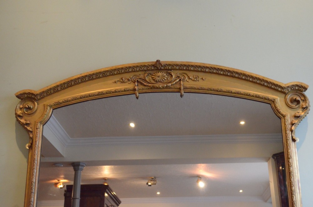 A large 19th-century English giltwood arched overmantel mirror featuring floral swag carvings at the crest and acanthus scroll feet at the base. View VII