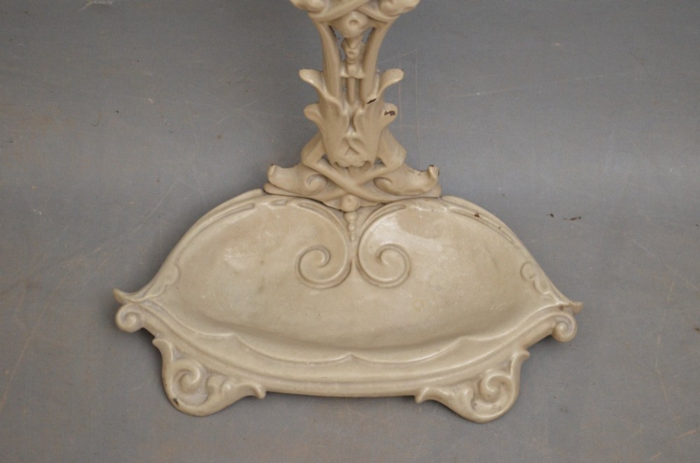 An Art Nouveau painted cream cast iron umbrella stand featuring organic scrollwork and an integrated drip tray at the base. View V