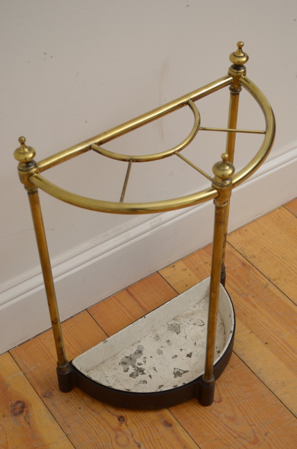 A Victorian half-moon brass umbrella stand featuring three tubular uprights topped with urn finials and a black cast-iron drip tray base. View II
