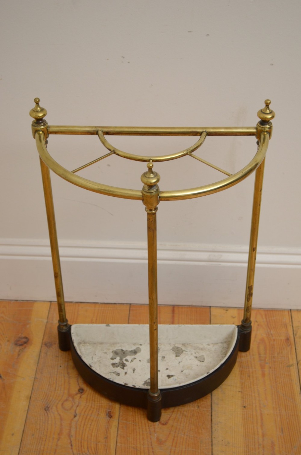A Victorian half-moon brass umbrella stand featuring three tubular uprights topped with urn finials and a black cast-iron drip tray base.