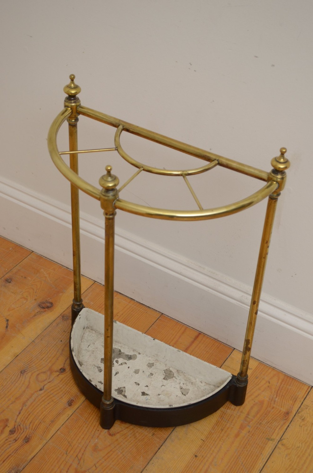 A Victorian half-moon brass umbrella stand featuring three tubular uprights topped with urn finials and a black cast-iron drip tray base. View III