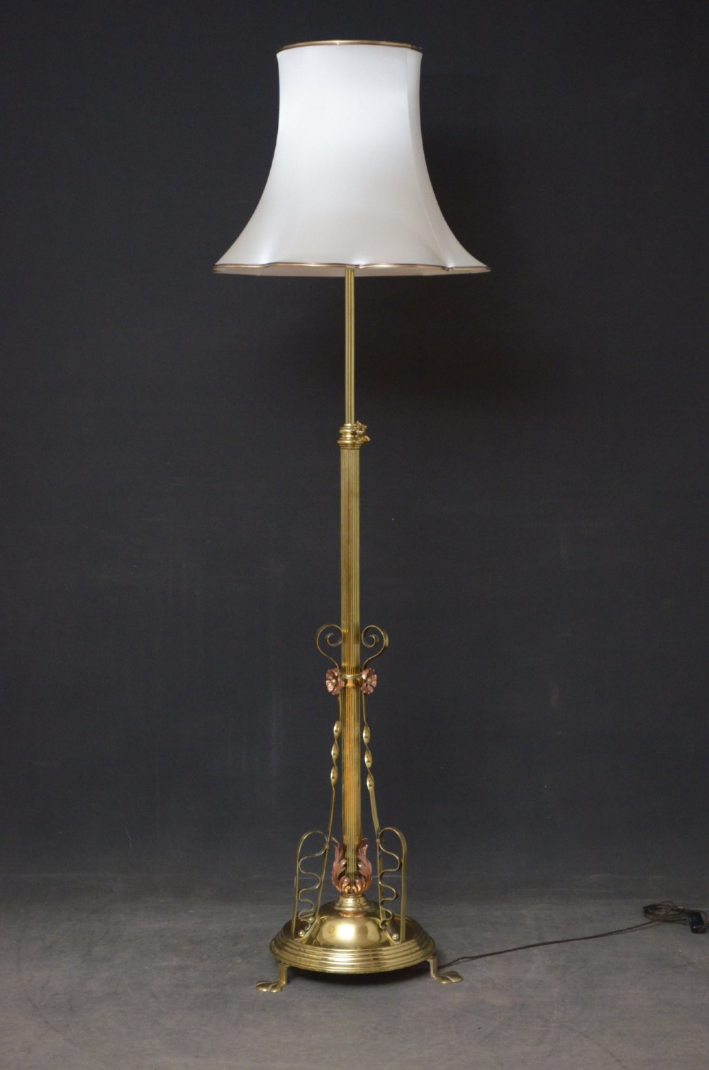 An Art Nouveau brass and copper standard lamp with a telescopic stem, scrolled metal base, and flared cream fabric shade. View X