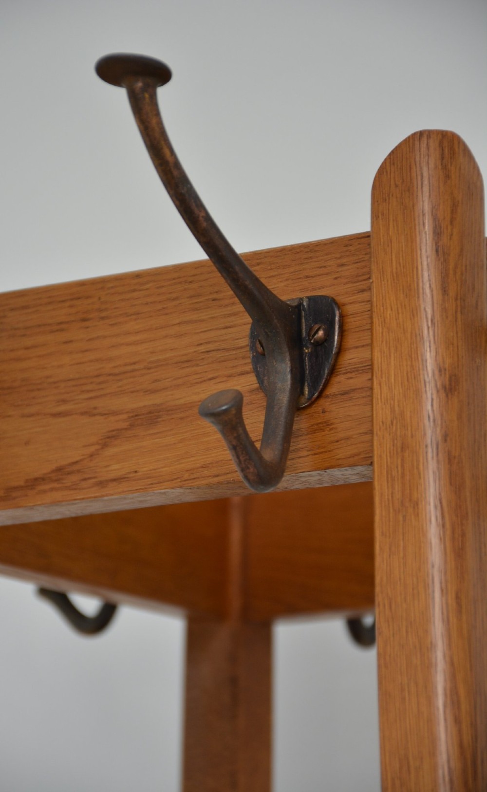 A tall, tapered oak coat stand featuring metal double hooks at the top, a square umbrella retaining rail in the centre, and a dark metal drip tray at the base. View III