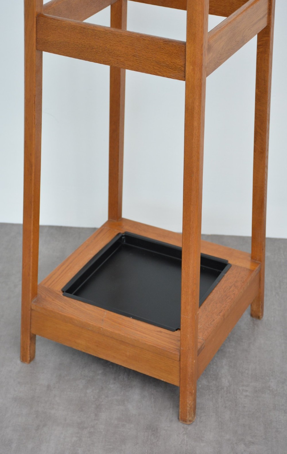 A tall, tapered oak coat stand featuring metal double hooks at the top, a square umbrella retaining rail in the centre, and a dark metal drip tray at the base. View VI
