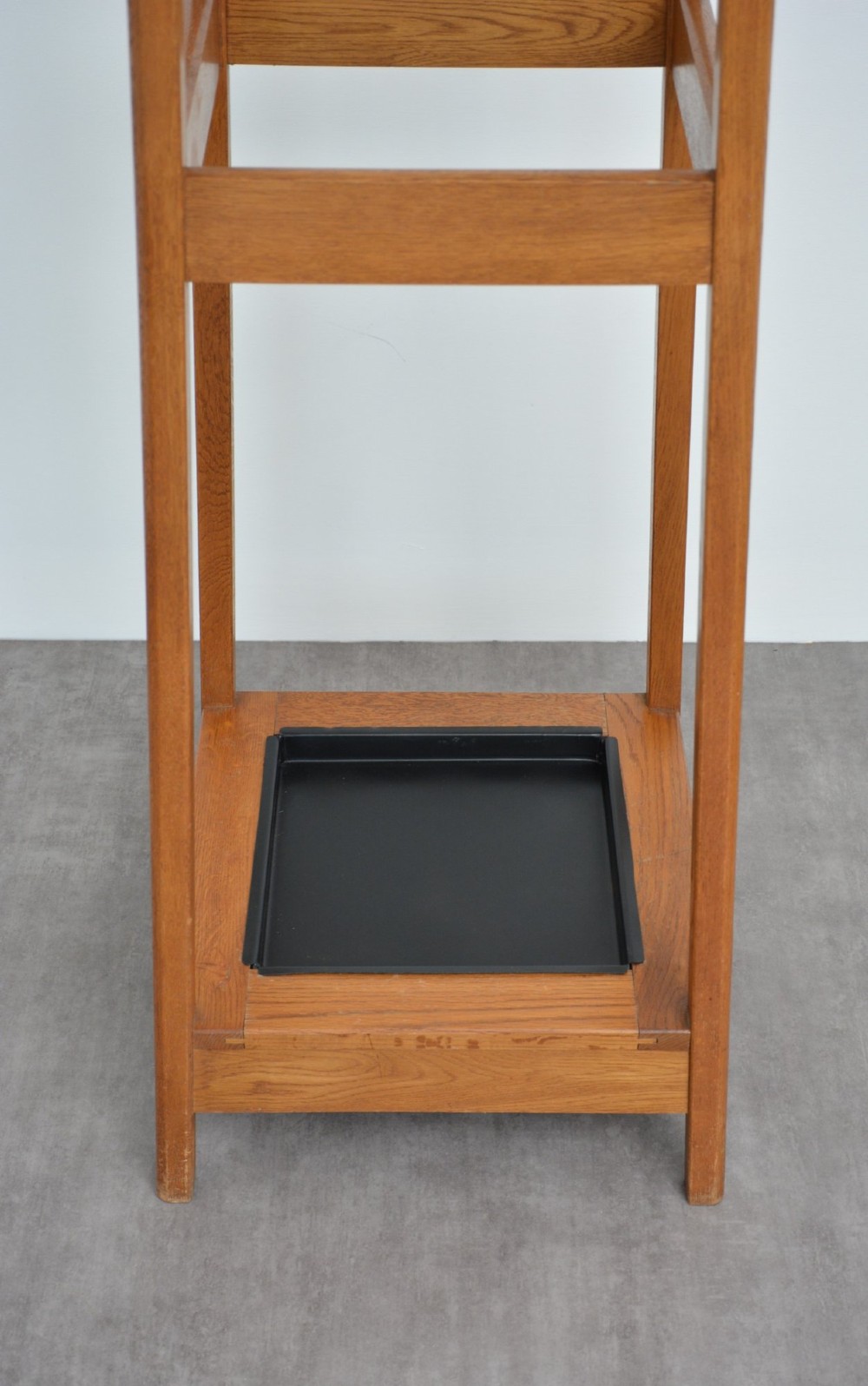 A tall, tapered oak coat stand featuring metal double hooks at the top, a square umbrella retaining rail in the centre, and a dark metal drip tray at the base. View VII