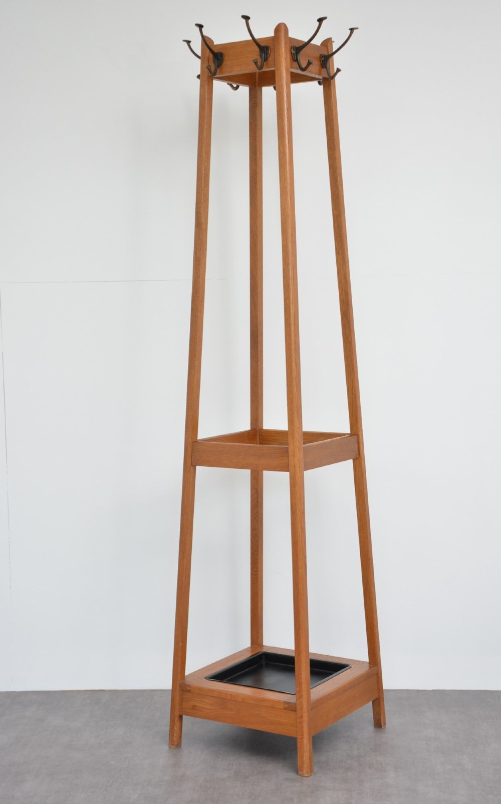 A tall, tapered oak coat stand featuring metal double hooks at the top, a square umbrella retaining rail in the centre, and a dark metal drip tray at the base. View IX