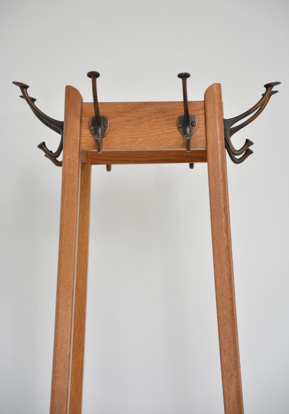 A tall, tapered oak coat stand featuring metal double hooks at the top, a square umbrella retaining rail in the centre, and a dark metal drip tray at the base. View XI