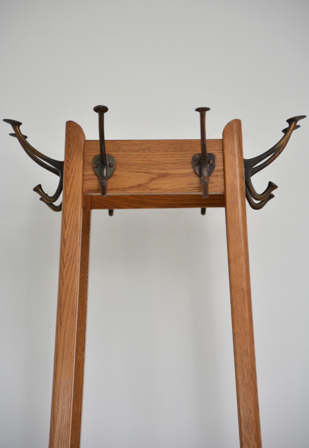 A tall, tapered oak coat stand featuring metal double hooks at the top, a square umbrella retaining rail in the centre, and a dark metal drip tray at the base. View XII