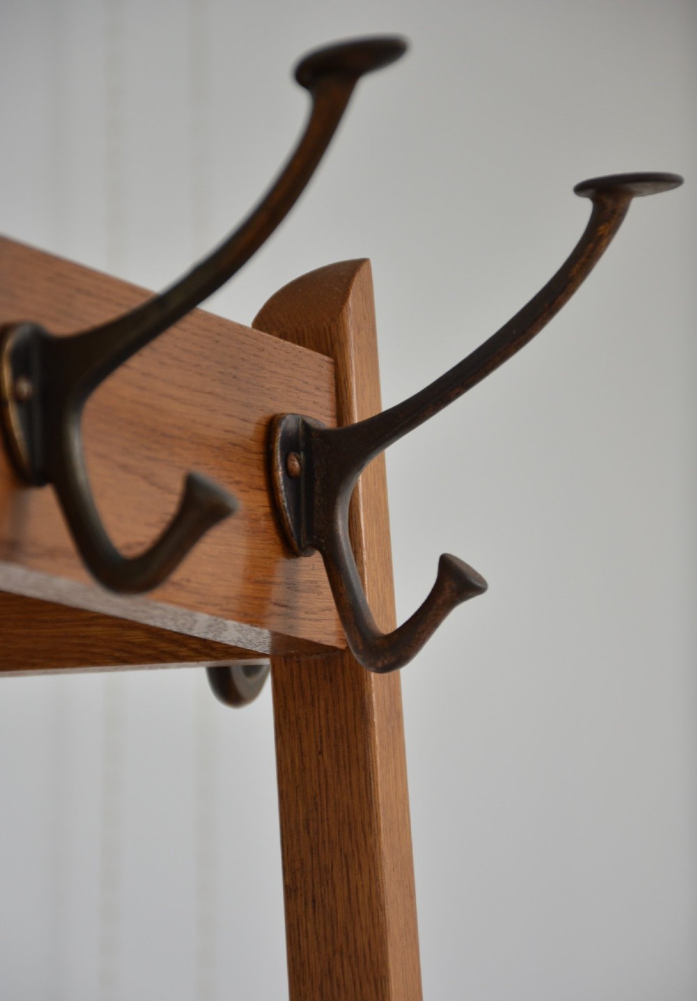 A tall, tapered oak coat stand featuring metal double hooks at the top, a square umbrella retaining rail in the centre, and a dark metal drip tray at the base. View XIV