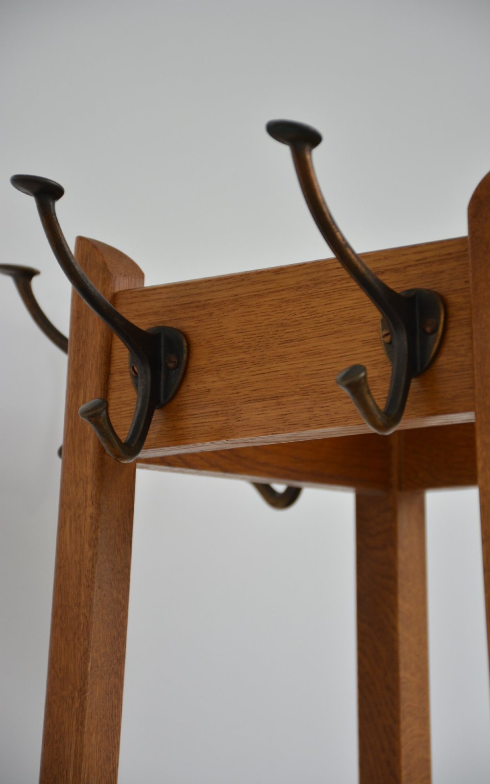 A tall, tapered oak coat stand featuring metal double hooks at the top, a square umbrella retaining rail in the centre, and a dark metal drip tray at the base. View XV