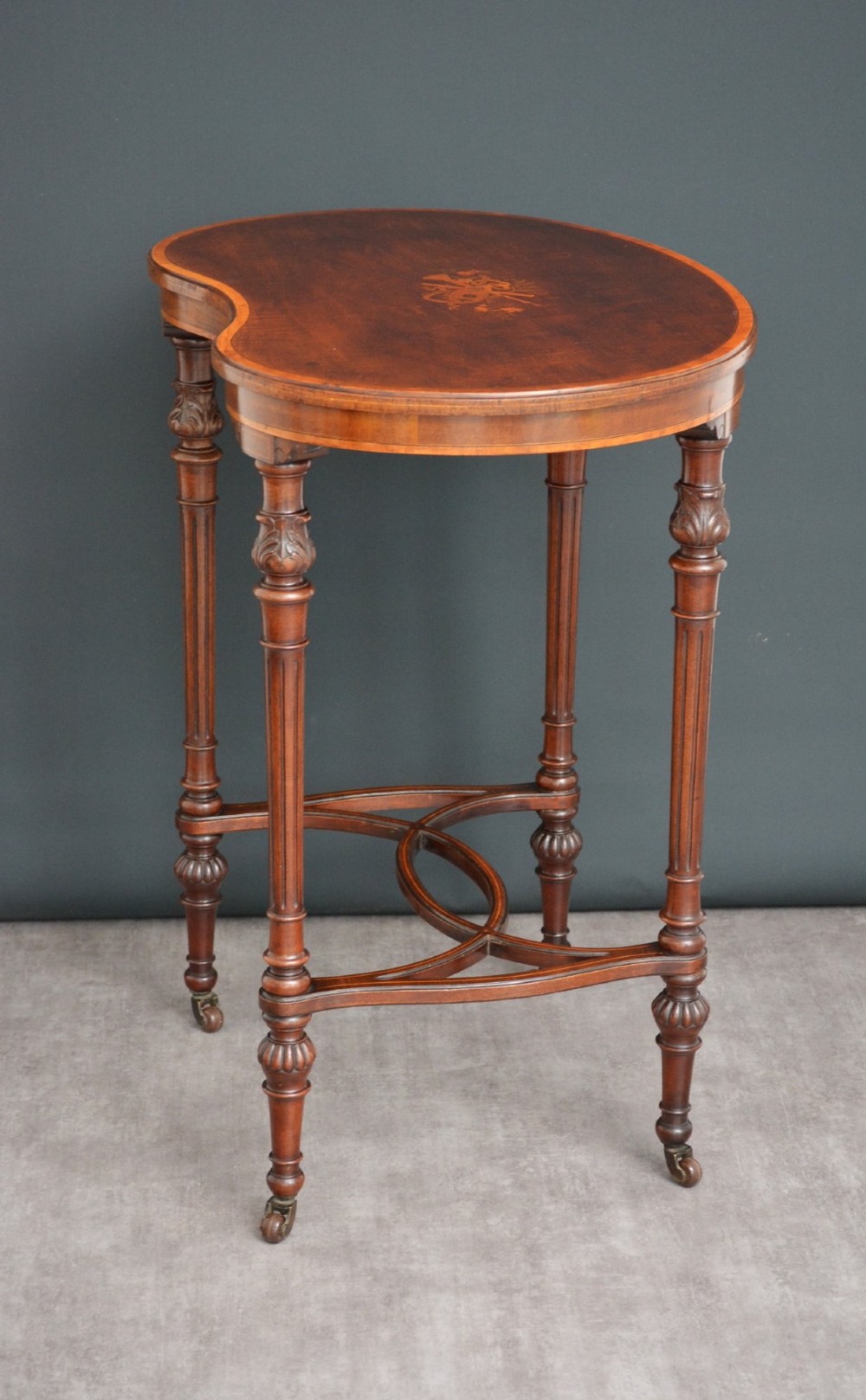 An Edwardian mahogany kidney-shaped side table featuring inlaid marquetry at the centre, fluted turned legs, a curved stretcher, and small brass castors. View II