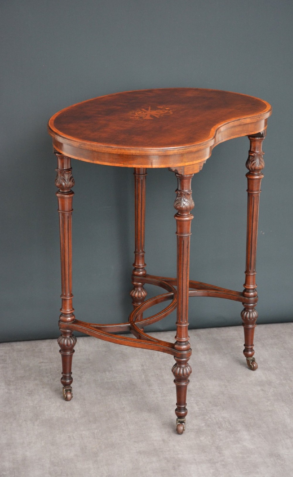 An Edwardian mahogany kidney-shaped side table featuring inlaid marquetry at the centre, fluted turned legs, a curved stretcher, and small brass castors. View IV