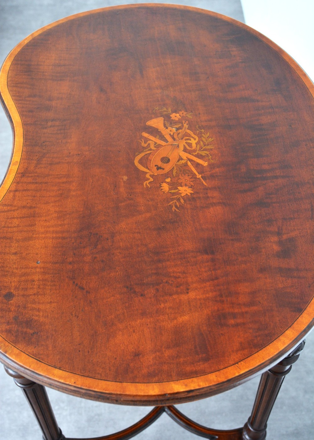 An Edwardian mahogany kidney-shaped side table featuring inlaid marquetry at the centre, fluted turned legs, a curved stretcher, and small brass castors. View V