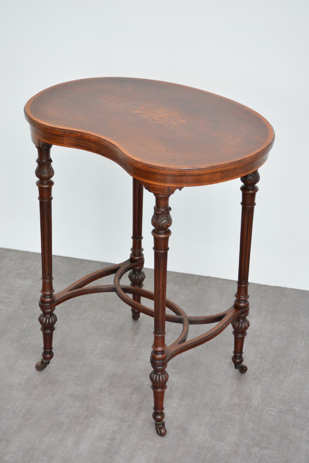 An Edwardian mahogany kidney-shaped side table featuring inlaid marquetry at the centre, fluted turned legs, a curved stretcher, and small brass castors. View XII