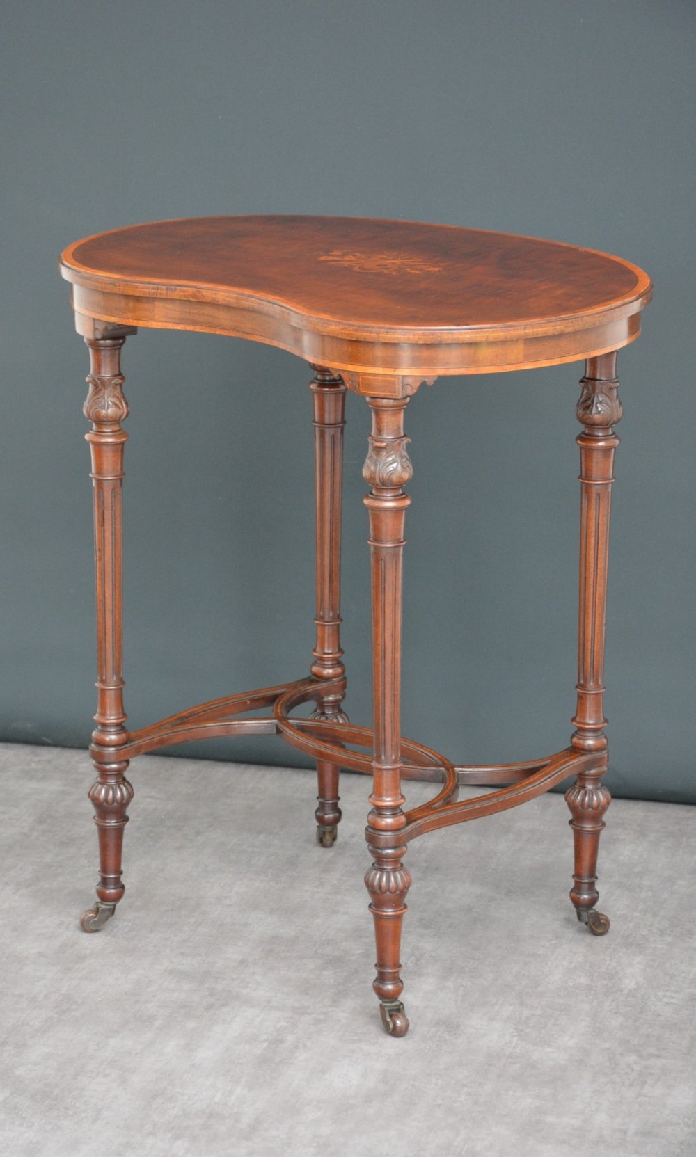 An Edwardian mahogany kidney-shaped side table featuring inlaid marquetry at the centre, fluted turned legs, a curved stretcher, and small brass castors. View XIV