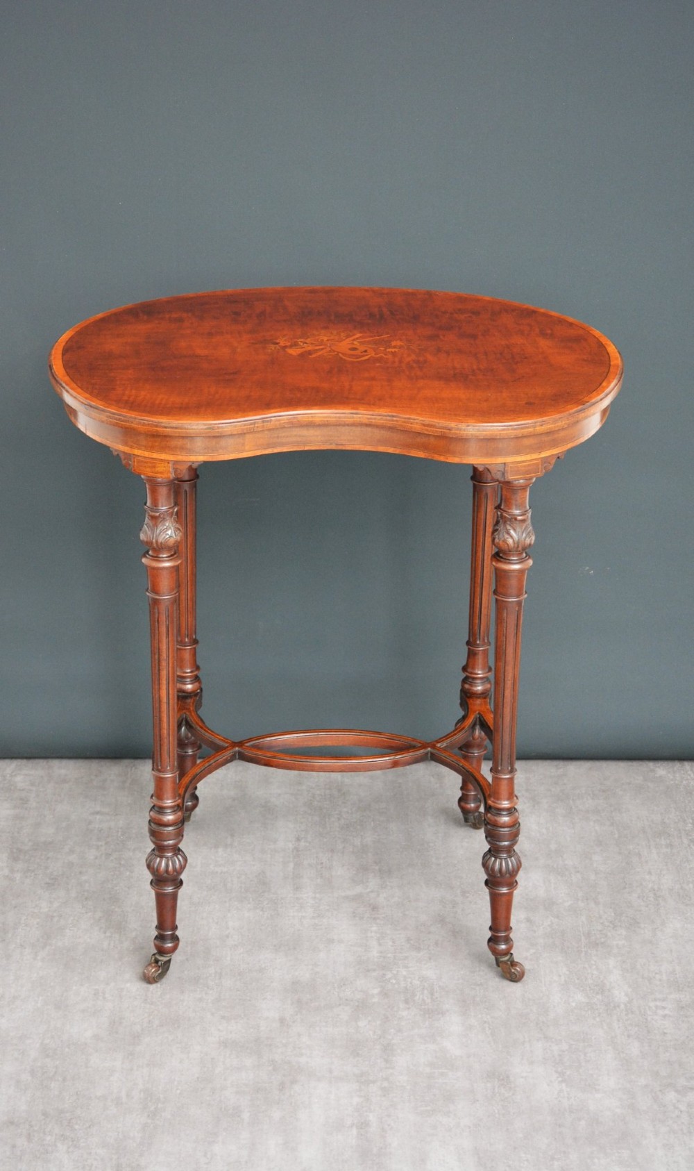 An Edwardian mahogany kidney-shaped side table featuring inlaid marquetry at the centre, fluted turned legs, a curved stretcher, and small brass castors. View XV
