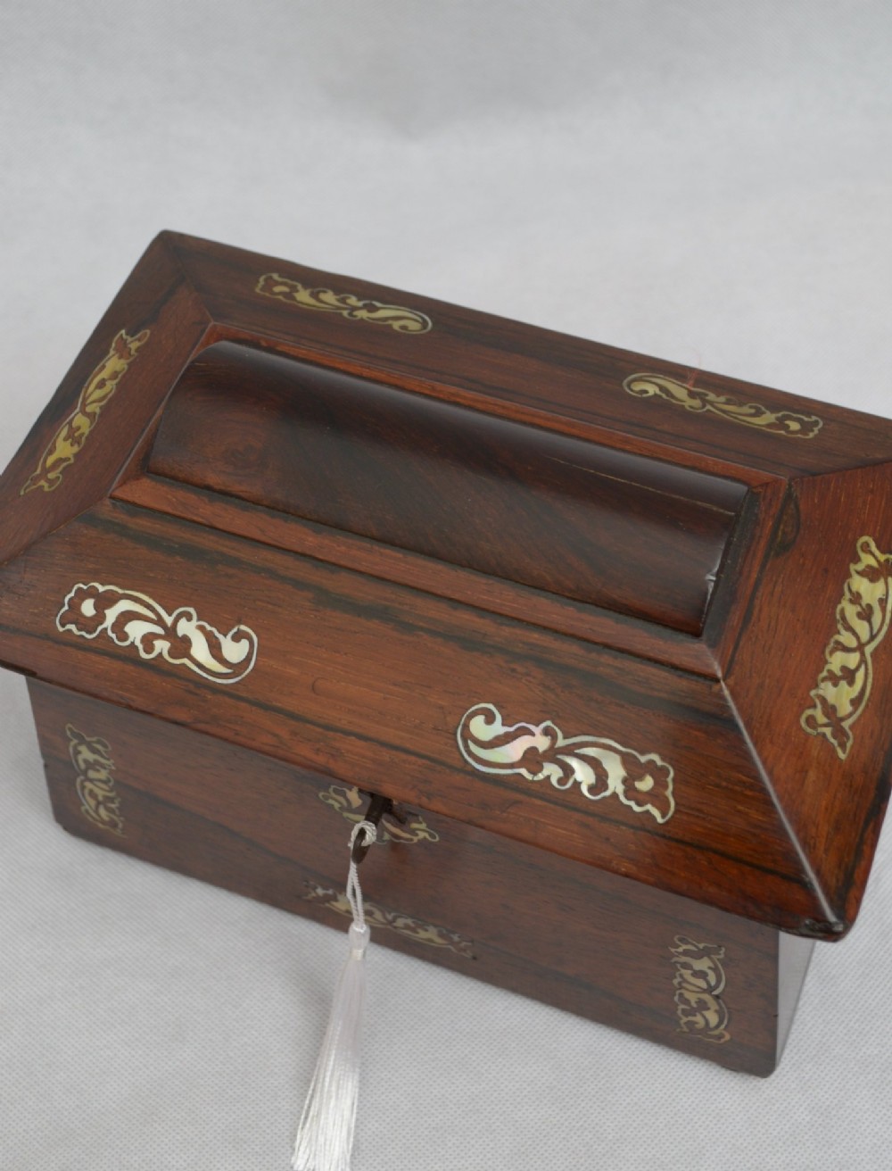 A Regency-era sarcophagus-shaped rosewood jewellery box featuring decorative scroll inlay and a key with a white tassel. View IV