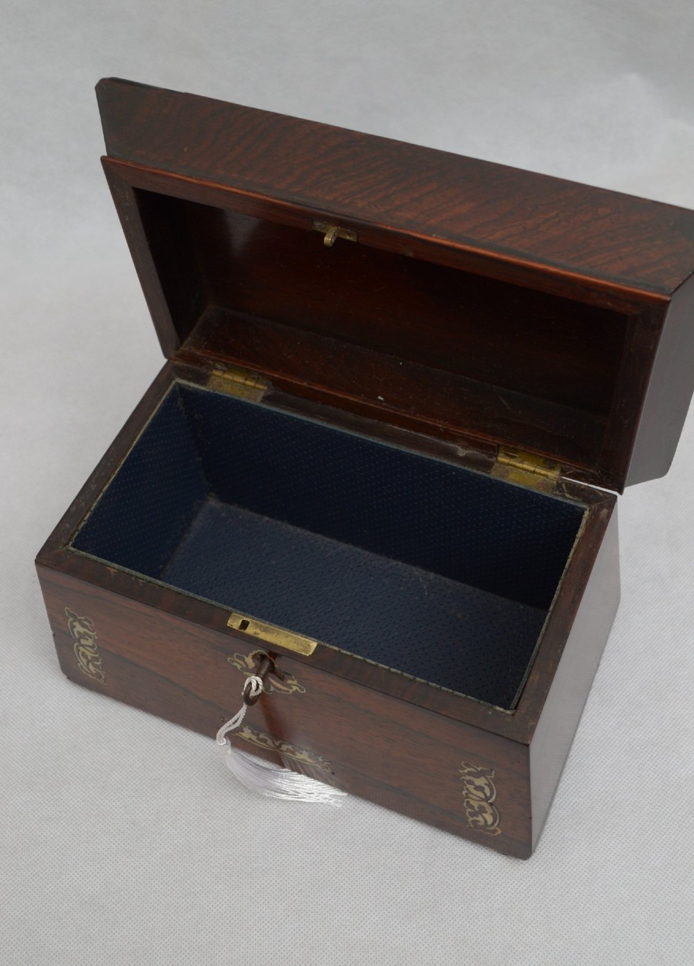 A Regency-era sarcophagus-shaped rosewood jewellery box featuring decorative scroll inlay and a key with a white tassel. View VI