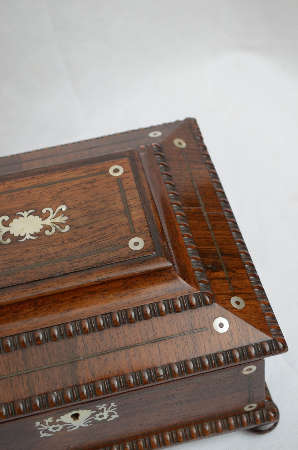 A William IV dark rosewood jewellery box featuring mother-of-pearl inlays, a tiered sarcophagus lid, carved gadrooned borders, and small bun feet. View X
