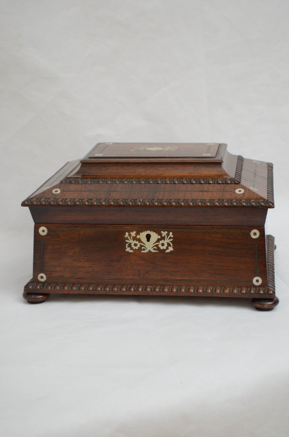 A William IV dark rosewood jewellery box featuring mother-of-pearl inlays, a tiered sarcophagus lid, carved gadrooned borders, and small bun feet. View XI