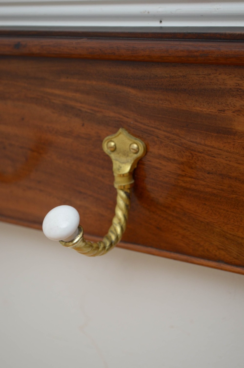 A wall-mounted mahogany coat rack featuring carved end scrolls and six brass rope-twist hooks with white ceramic knobs. View II