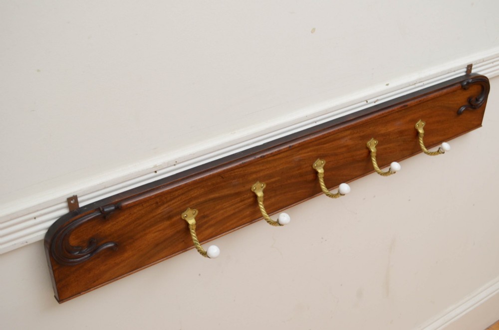 A wall-mounted mahogany coat rack featuring carved end scrolls and six brass rope-twist hooks with white ceramic knobs. View IV