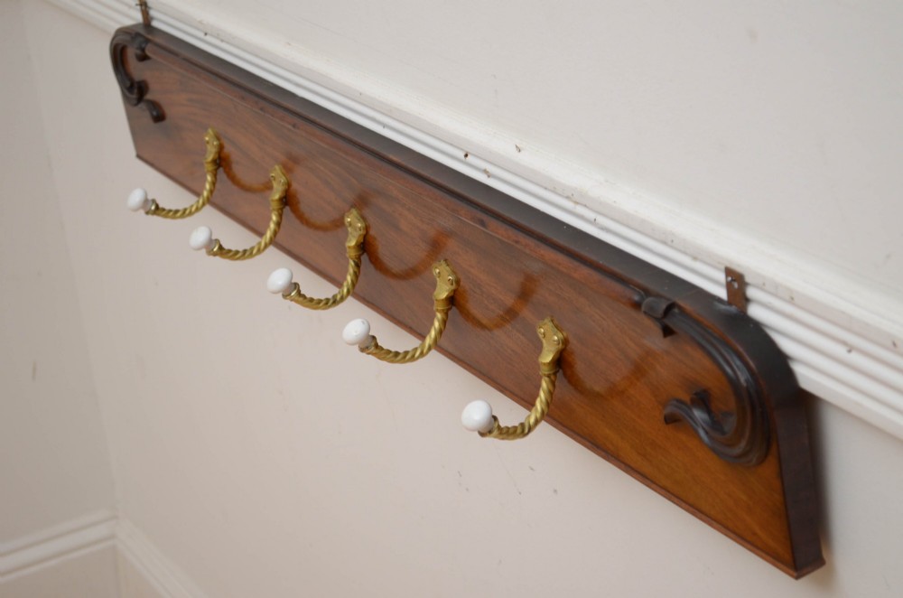 A wall-mounted mahogany coat rack featuring carved end scrolls and six brass rope-twist hooks with white ceramic knobs. View V