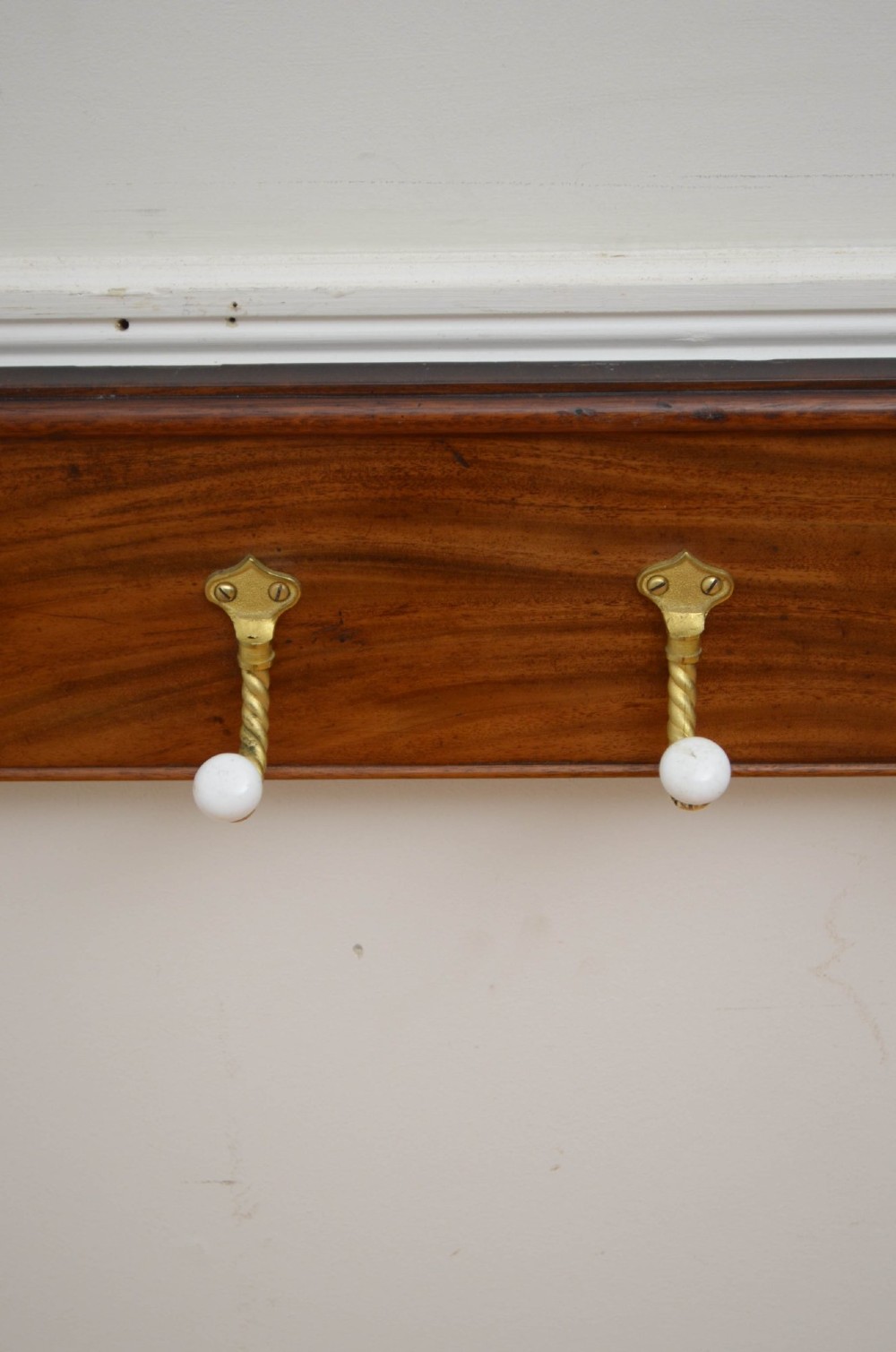 A wall-mounted mahogany coat rack featuring carved end scrolls and six brass rope-twist hooks with white ceramic knobs. View VII