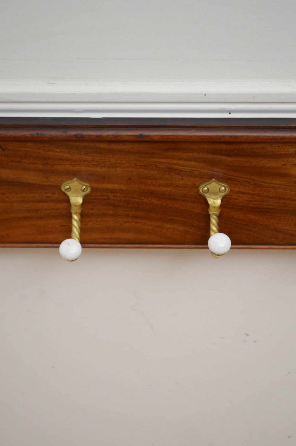 A wall-mounted mahogany coat rack featuring carved end scrolls and six brass rope-twist hooks with white ceramic knobs. View VIII