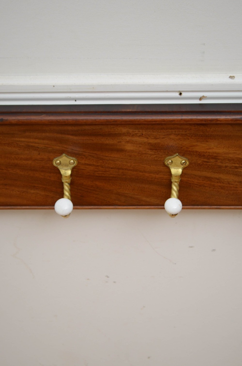A wall-mounted mahogany coat rack featuring carved end scrolls and six brass rope-twist hooks with white ceramic knobs. View IX
