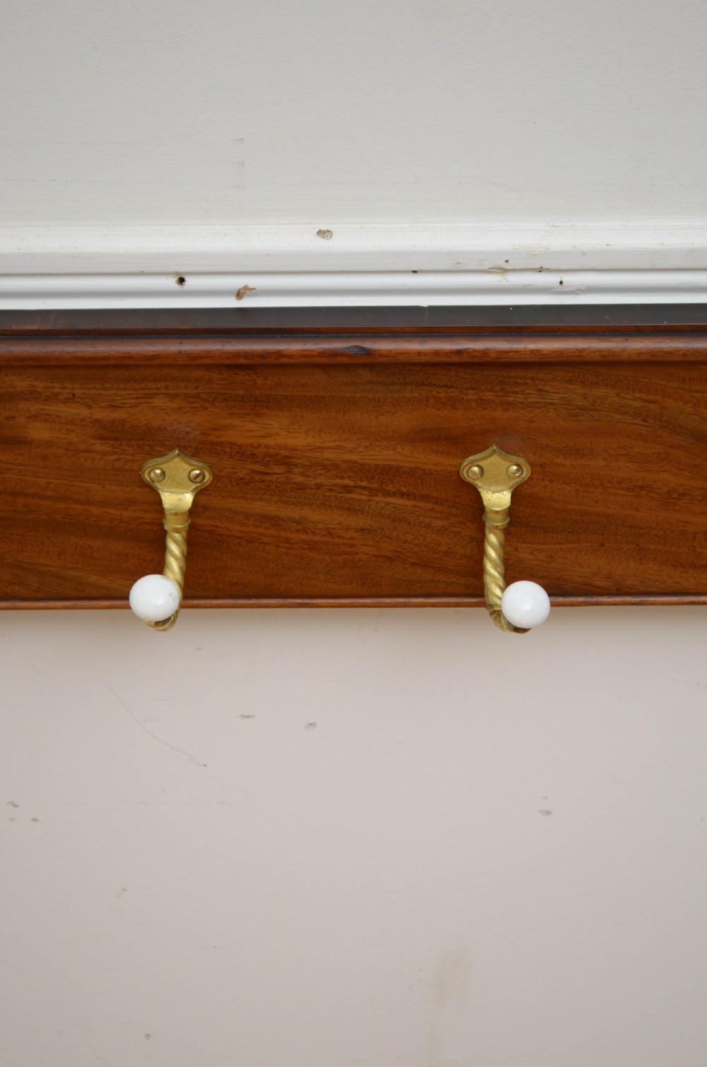 A wall-mounted mahogany coat rack featuring carved end scrolls and six brass rope-twist hooks with white ceramic knobs. View X