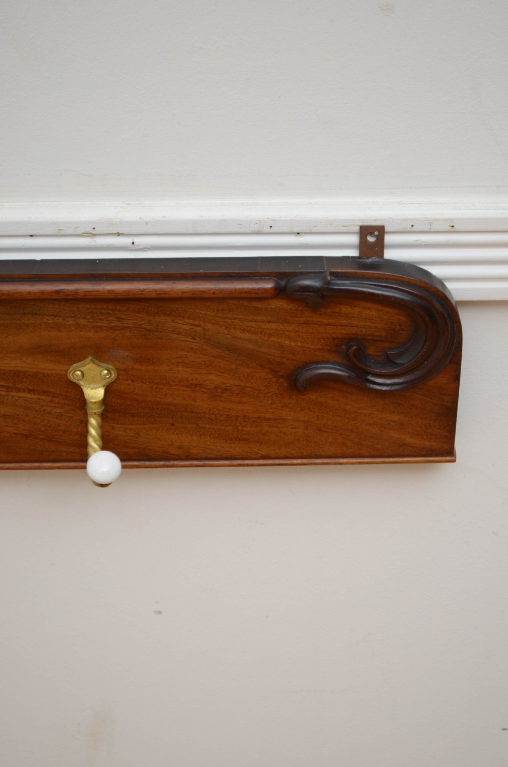 A wall-mounted mahogany coat rack featuring carved end scrolls and six brass rope-twist hooks with white ceramic knobs. View XI