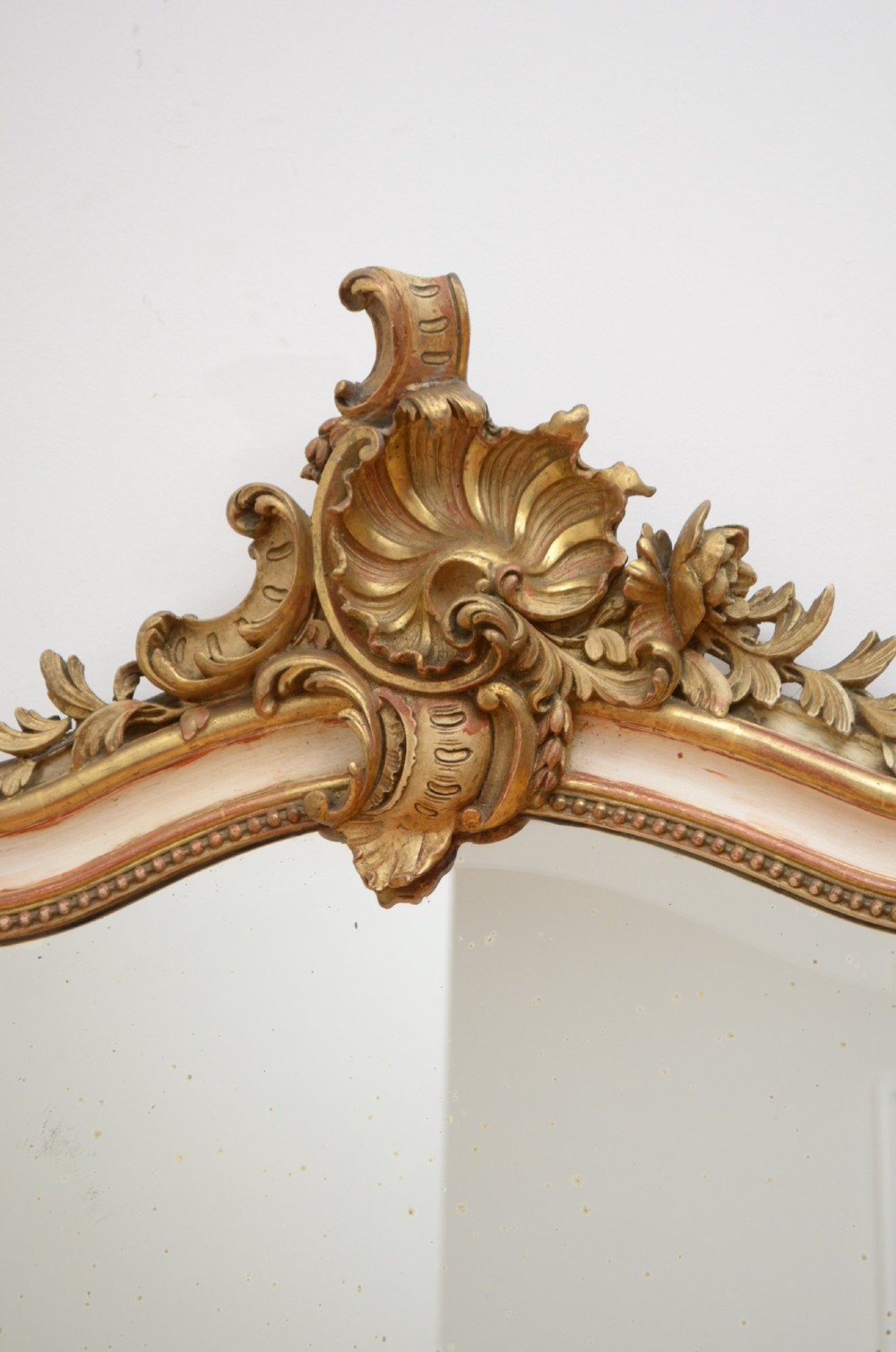 A tall 19th-century French wall mirror with a gilded gesso frame, arched top, ornate shell cresting, and mild foxing across the mirror plate. View VI