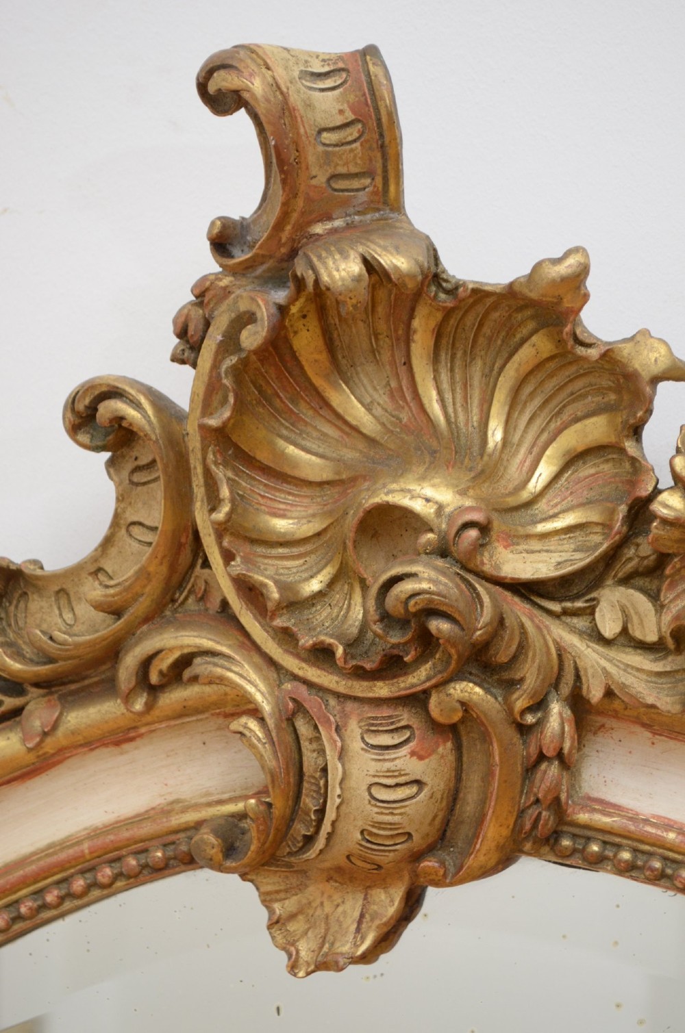 A tall 19th-century French wall mirror with a gilded gesso frame, arched top, ornate shell cresting, and mild foxing across the mirror plate. View VIII