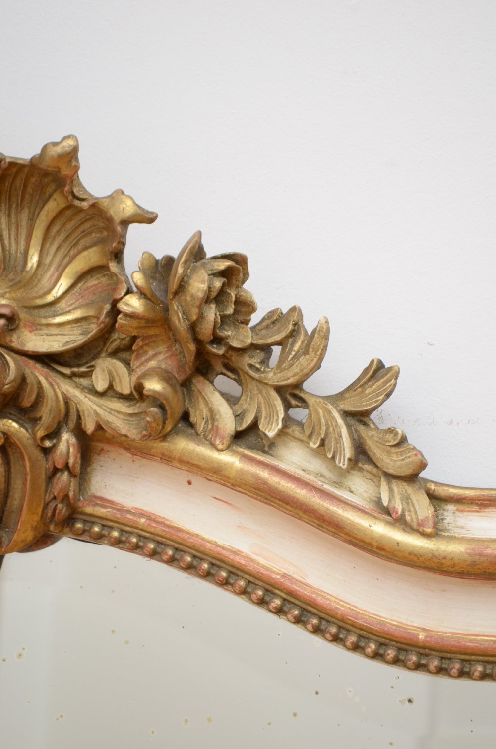 A tall 19th-century French wall mirror with a gilded gesso frame, arched top, ornate shell cresting, and mild foxing across the mirror plate. View IX
