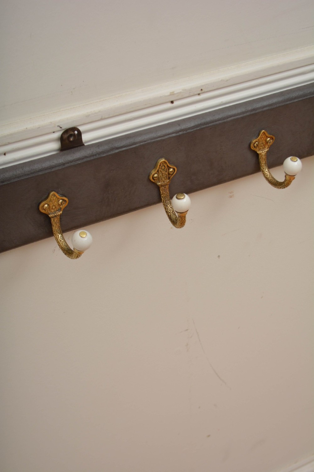 A wall-mounted grey wooden rail fitted with multiple cast brass coat hooks featuring white ceramic ball tips. View II