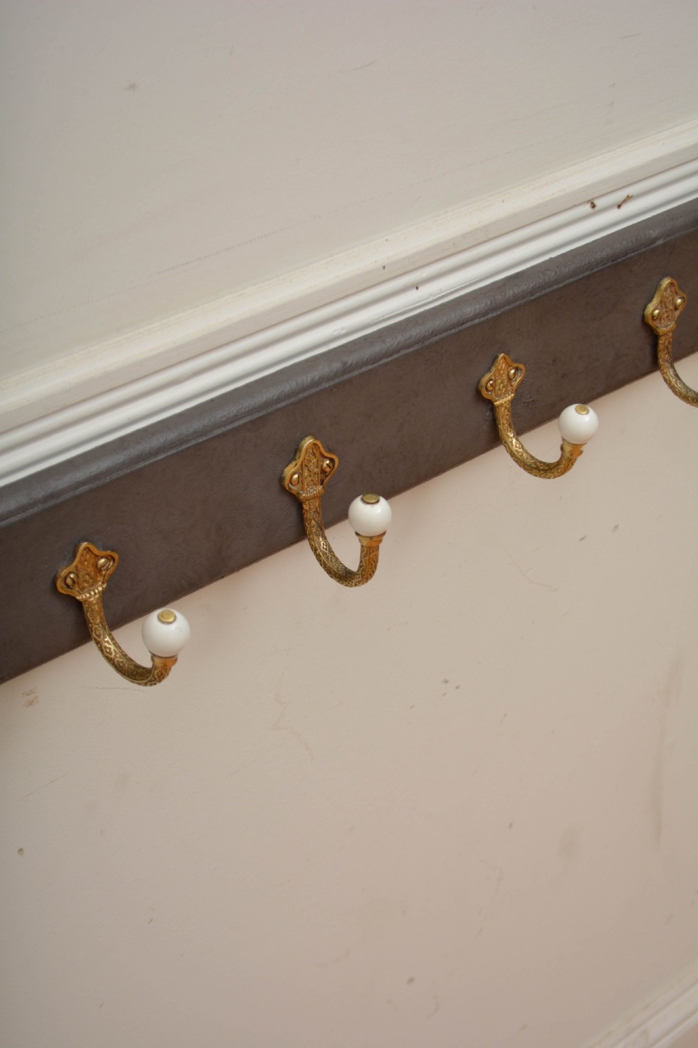 A wall-mounted grey wooden rail fitted with multiple cast brass coat hooks featuring white ceramic ball tips. View III